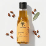 A bottle of Wild Organic Jojoba Oil with a black cap, surrounded by scattered coffee beans and a single green leaf on a clean white background.